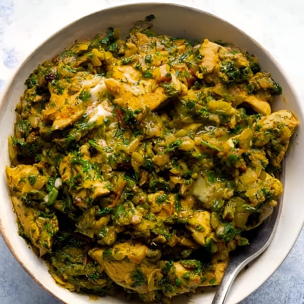 Close-up of Tandoor Indian Cuisine's chicken dish with green herbs and spices in a white bowl.