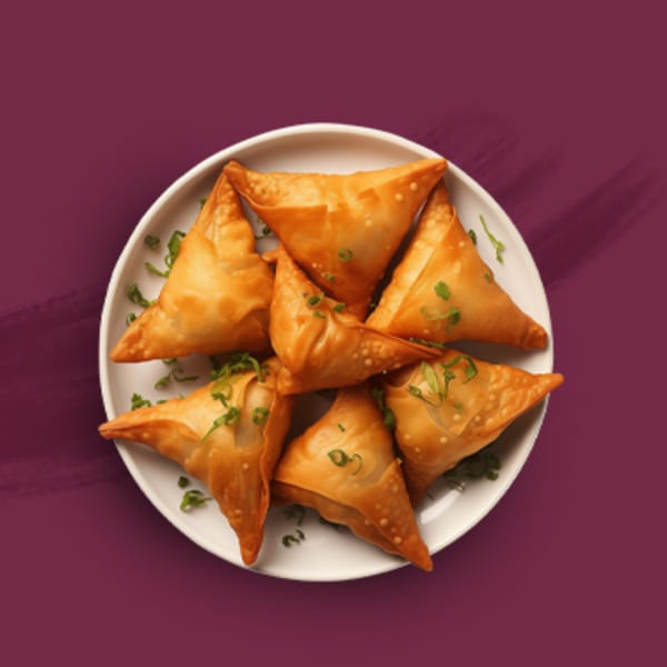 A white plate filled with golden-brown, triangular samosas garnished with fresh green herbs on a purple background.