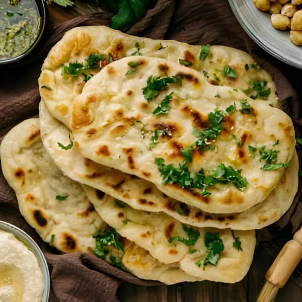 Stack of golden-brown naan bread, garnished with fresh green cilantro, on a brown cloth.