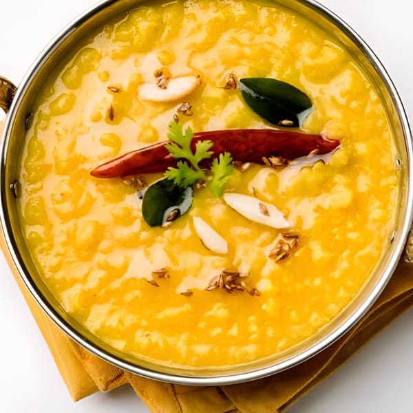 A close-up of Tandoor Indian Cuisine's yellow dal in a metal bowl, garnished with chili and cilantro.