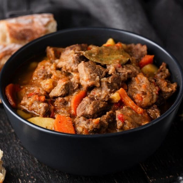 A black bowl filled with Tandoor Indian Cuisine's beef stew, carrots, potatoes, and bay leaf.