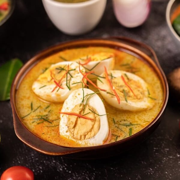 Indian egg curry with sliced hard-boiled eggs in a rich yellow sauce, garnished with herbs and chili.